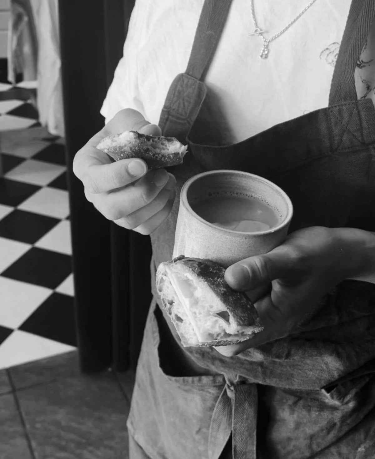 Baker in an apron holding a sandwich and a cup of coffee