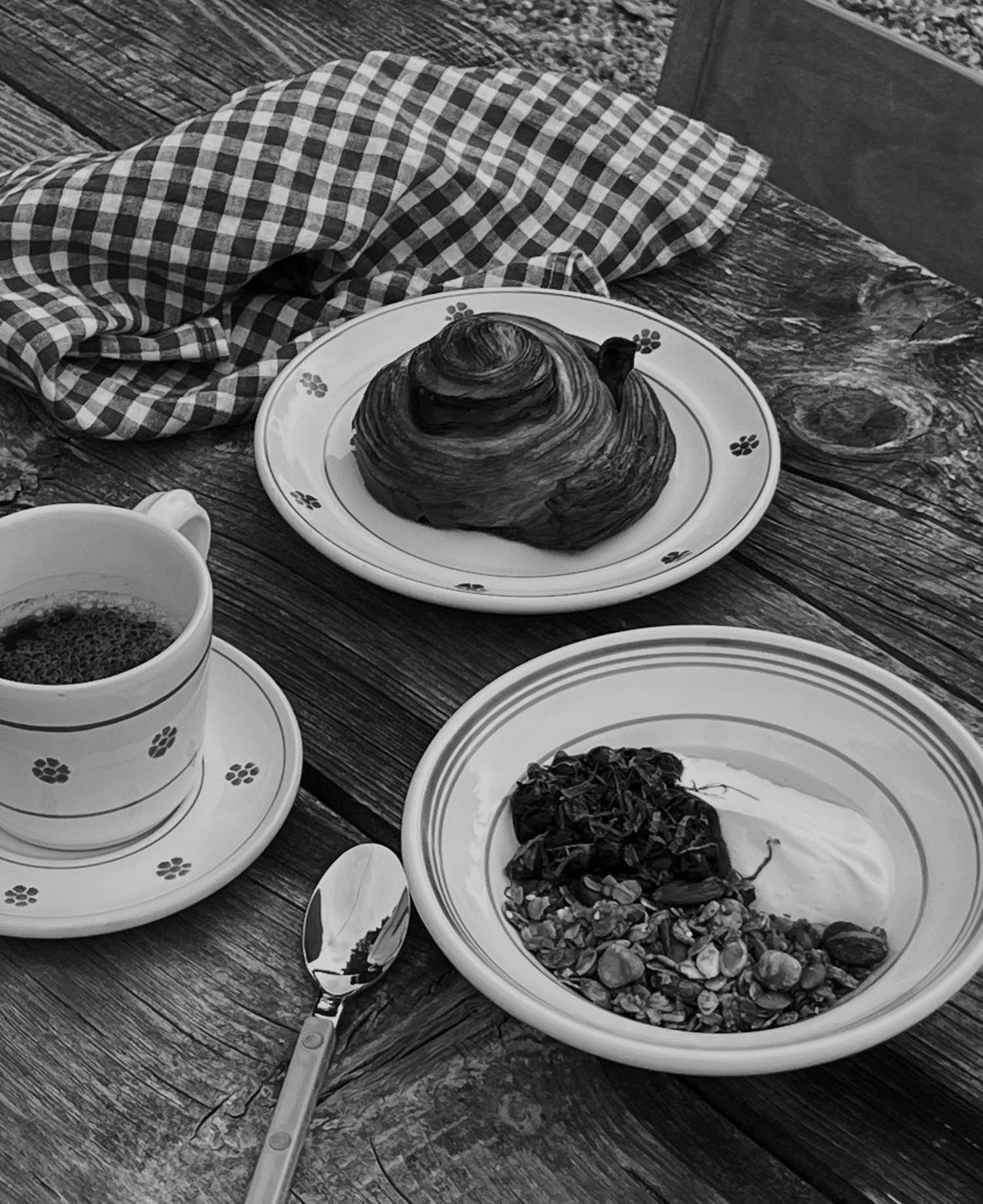 Breakfast on a wooden deck — cinnamon bun, coffee and yoghurt with granola