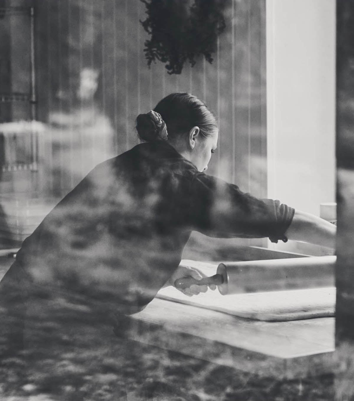 Woman rolling out dough, seen through a window